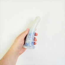 Load image into Gallery viewer, A hand holds a 6 inch curved ceramic dildo in a dark blue to light blue speckle pattern against a white background.