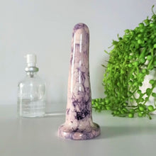 Load image into Gallery viewer, A 4 inch classic ceramic dildo in a pink and dark purple bubble pattern stands on a white table against a white background. A glass bottle of Uberlube is to the left in background, while a bright green pot plant flows from a white pot to the right.