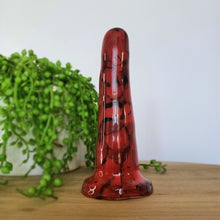 Load image into Gallery viewer, A 5 inch classic ceramic dildo in red with a black bubble pattern stands on a wooden table. A bright green plant flows from a white pot in the background.
