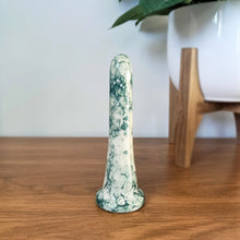 Load image into Gallery viewer, A 6 inch classic ceramic dildo in a dark green bubble pattern stands on a wooden table against a white background. A plant in a white pot with a wooden stand is to the right.