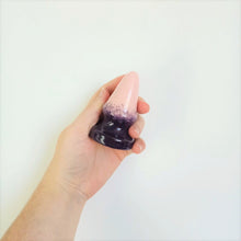 Load image into Gallery viewer, A hand holds a 3 inch cone shaped ceramic butt plug in a dark purple to pink gradient pattern in front of a white wall.
