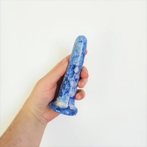 A hand holds a 5 inch classic ceramic dildo in a dark blue and light blue bubble pattern in front of a white background.
