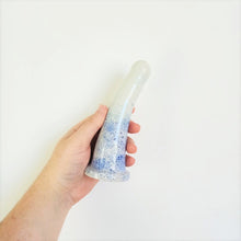 Load image into Gallery viewer, A hand holds a 6 inch curved ceramic dildo in a dark blue to light blue speckle pattern against a white background.
